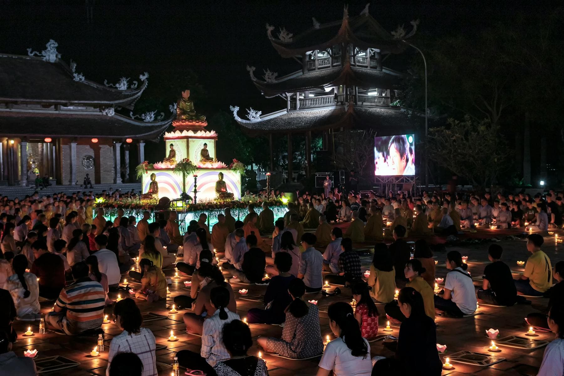 Vietnamese Buddhist Vesak ceremony at night — practitioners with candles before a Buddha altar at a pagoda, Phật Đản observance in Vietnam.