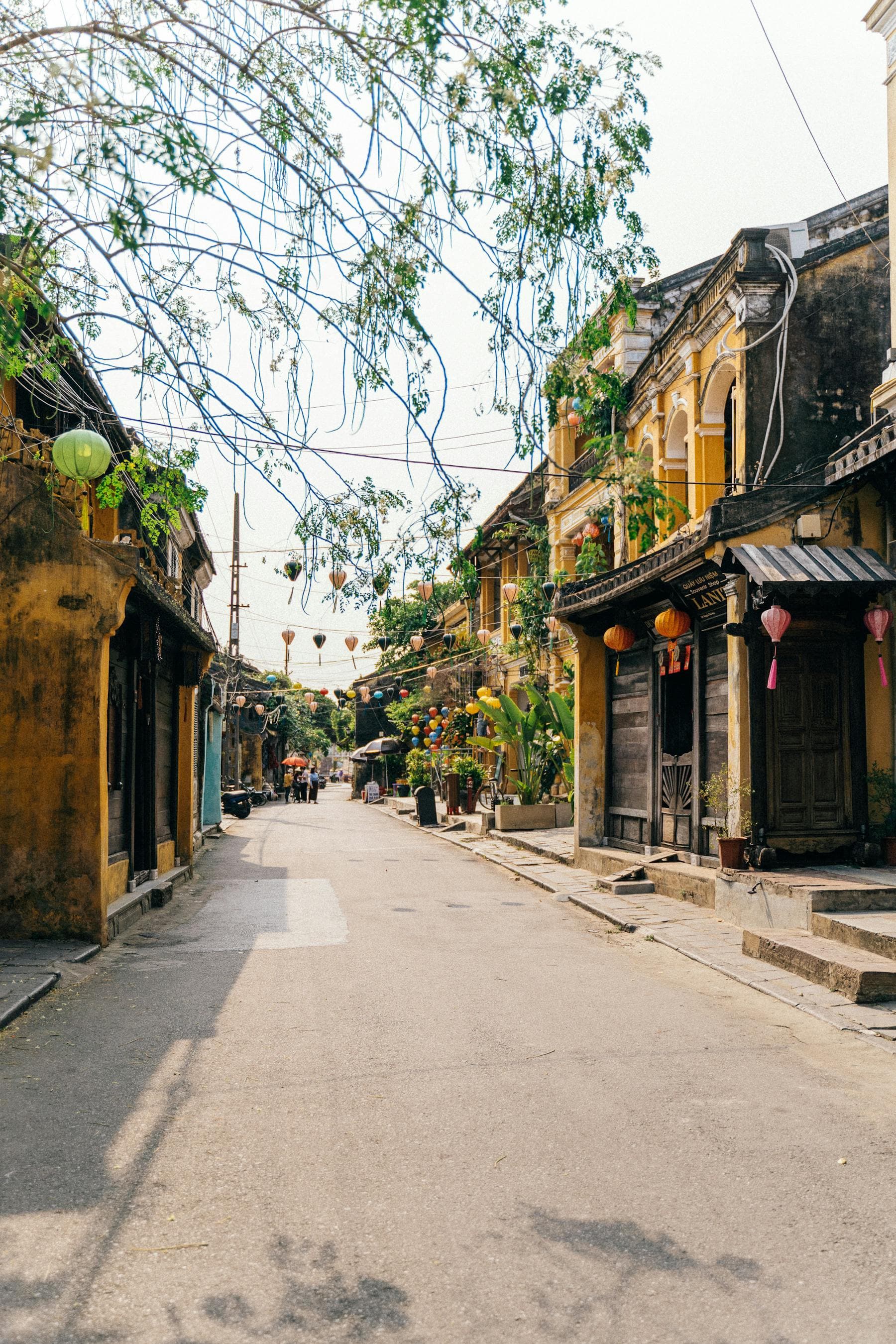 Hội An Old Town pedestrian street at midday with yellow ochre French-colonial merchant houses, hanging silk lanterns, and the empty cobblestone lane — central Vietnam UNESCO heritage core