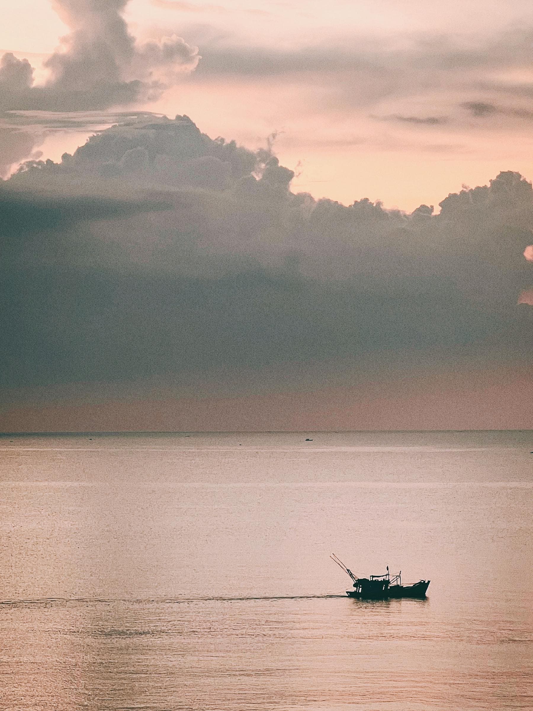 Sunset over the Thu Bồn river at Hội An, a boat silhouetted on gold water — the riverside setting for a slow four-day honeymoon, from Nghê Prana at Cẩm Nam.